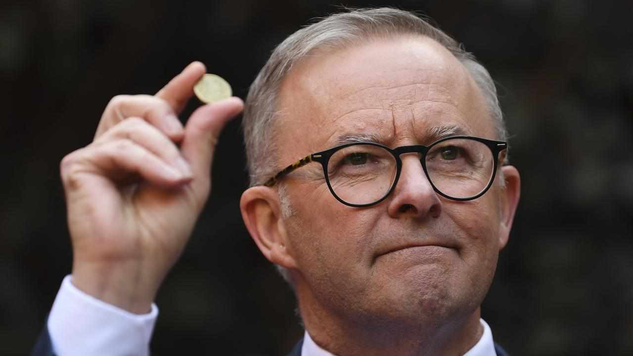 Anthony Albanese holds a one dollar coin.
